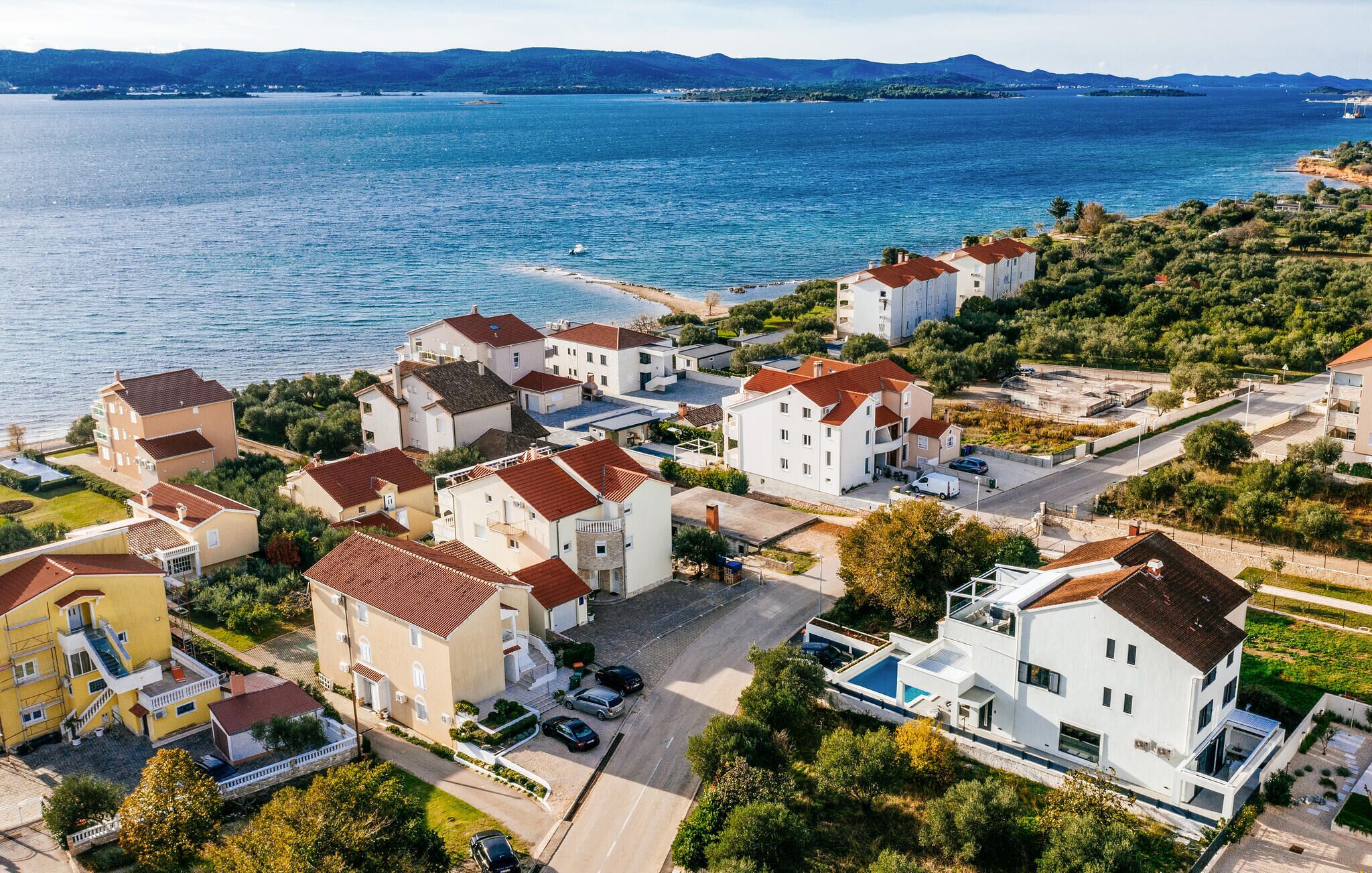 Ett bostadsområde vid kusten med hus som har röda tegeltak och vita väggar, fri utsikt över havet och en liten strand.