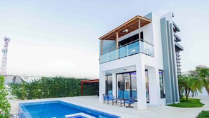 Un edificio moderno de dos pisos con piscina, mobiliario exterior y vista a un puente.