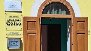 Un edificio amarillo con puerta de madera y una ventana. Hay carteles en la pared con información de contacto y números de habitación.