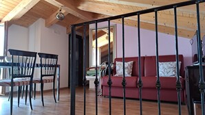 Una sala de estar con un sofá rojo, una mesa de comedor de madera y sillas, y una barandilla de metal negro.