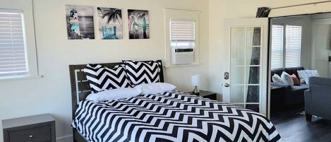 A bedroom with a bed, bedside tables, a nightstand, a sofa, and a door leading to another room.