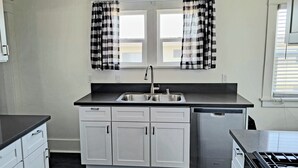 A compact kitchen with a double sink, white cabinets, a black countertop, and a built-in dishwasher. - Modern 2 bed 2 bath Paradise - Mins. from LAX & SOFI (Los Angeles)