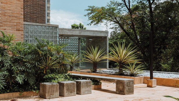 Un patio con un banco de hormigón, plantas en macetas y un edificio con fachada de vidrio.