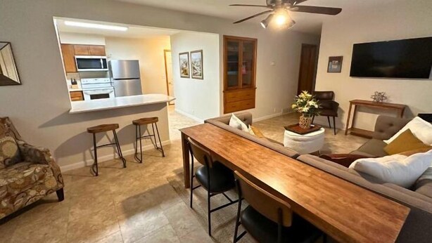 Un salon moderne avec une table à manger en bois, des tabourets de bar, un canapé et un coin cuisine équipé d’un réfrigérateur et d’un four à micro-ondes.