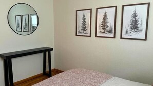 Une chambre à coucher comprenant un lit, une table de chevet, un miroir et trois tableaux encadrés accrochés au mur.