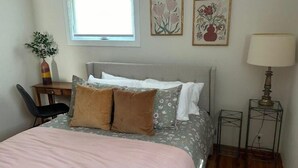 Une chambre à coucher avec un lit, un bureau, une chaise, une lampe et des œuvres d’art accrochées au mur.