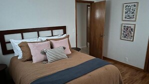 Une chambre à coucher avec un lit, des oreillers, une table de chevet et une porte donnant sur une autre pièce.