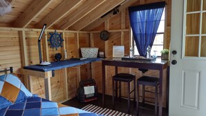 Una cabaña acogedora con interior de madera, un escritorio con dos taburetes, un reloj y una ventana con cortinas azules.