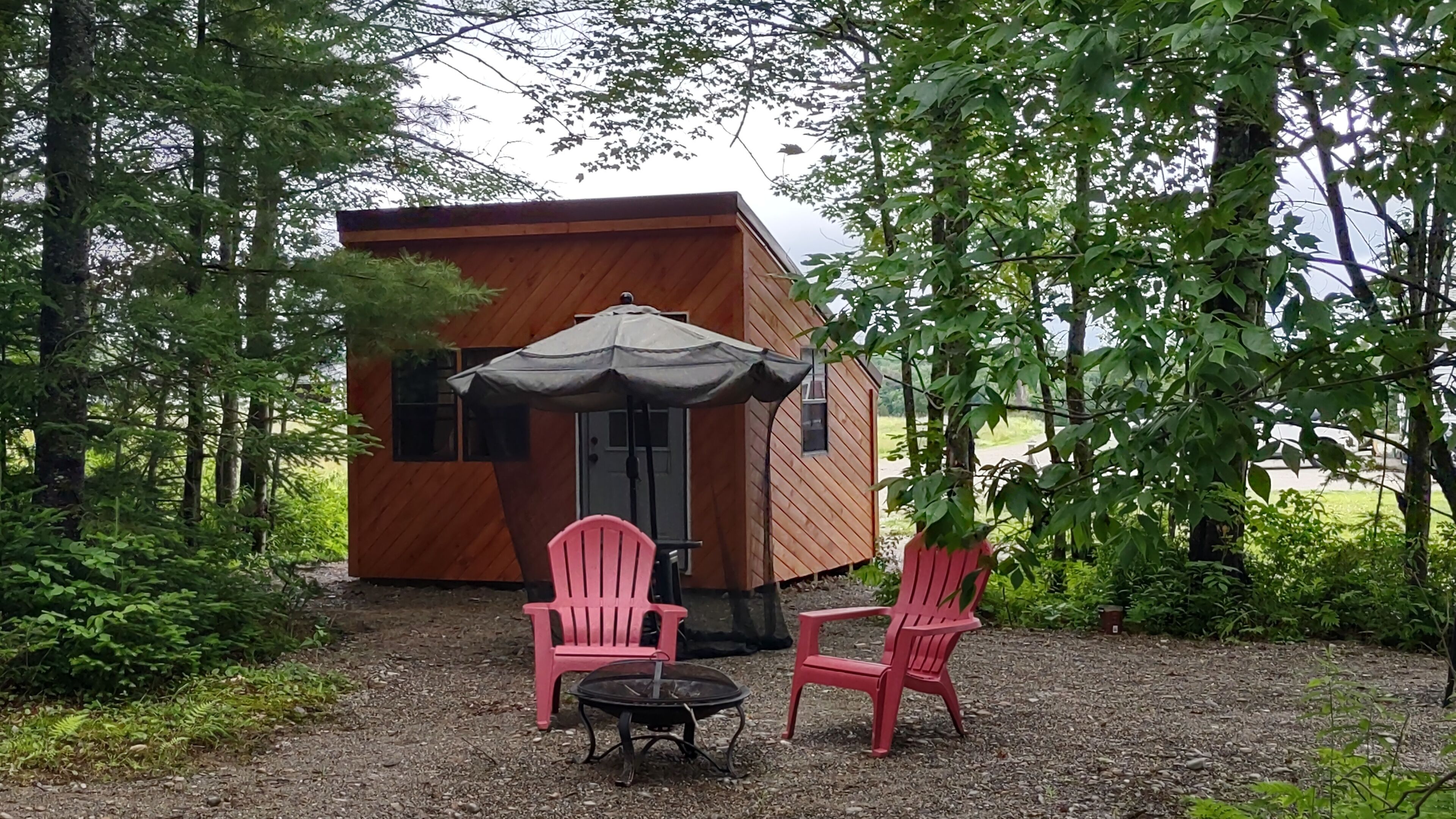 Una cabaña de madera con un pequeño patio, dos sillas rojas y una mesa.