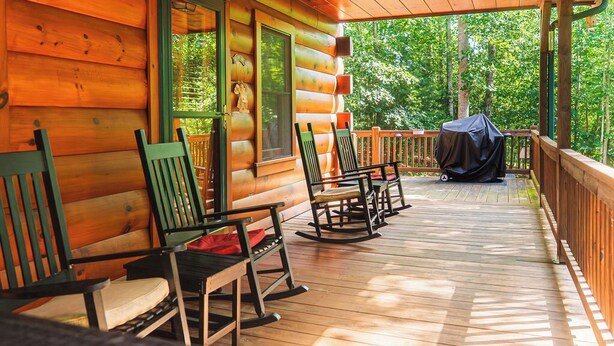 Une cabane en bois dotée d’un porche avec des fauteuils à bascule et d’un espace barbecue couvert.
