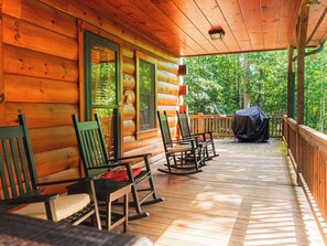 Une cabane en bois dotée d’un porche avec des fauteuils à bascule et d’un espace barbecue couvert.