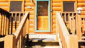 Une cabane en bois avec une porte centrale, deux fenêtres et un escalier en bois menant à l’entrée.
