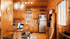 L’intérieur d’un chalet en bois comprend un coin cuisine avec une table à manger, des chaises, un réfrigérateur et un buffet en bois.