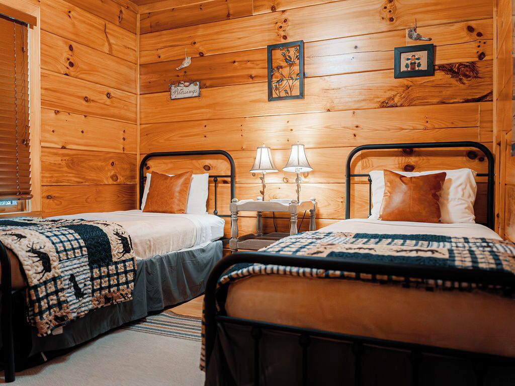 Habitació de cabana de fusta amb dos llits, cadascun amb un llençol acolxat, dues làmpades de nit i una taula petita entre els llits.