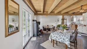Un vaste espace de vie doté d’un haut plafond, une table à manger recouverte d’une nappe à motifs floraux et un coin salon confortable avec un canapé et des fauteuils.