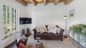 Un salon avec un canapé en cuir marron, un téléviseur à écran plat fixé au mur, une grande fenêtre à carreaux et un lampadaire.