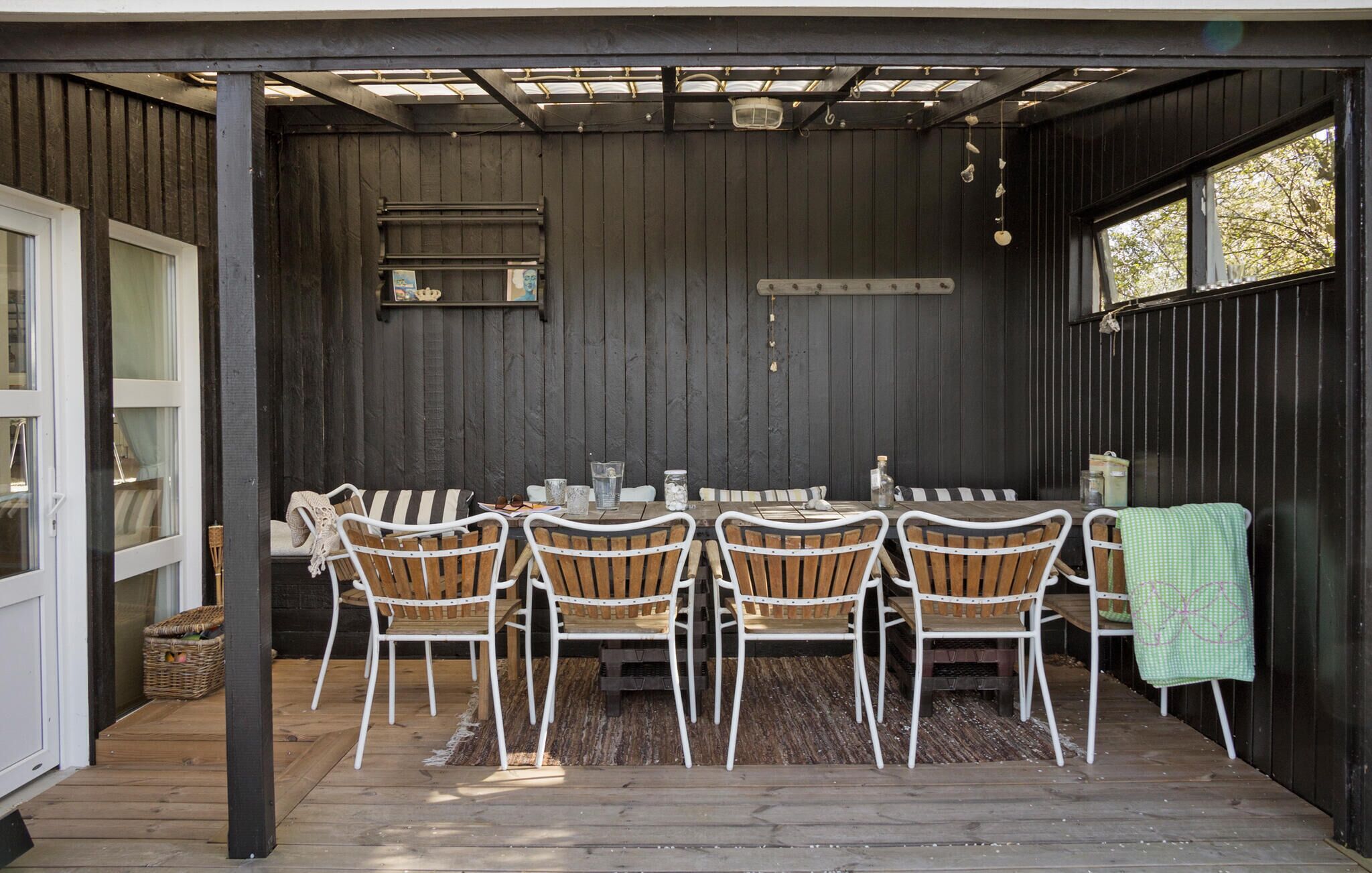 An outdoor dining area with a wooden table and chairs, a pergola overhead, and a view of the surrounding trees.