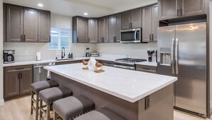 Une cuisine moderne avec des meubles de couleur bois foncé, un réfrigérateur en acier inoxydable, un four à micro-ondes et un grand îlot central doté de tabourets de bar.