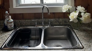 A kitchen with a double sink, a window with a view of a lake, and a vase with white flowers on the counter. - Lake Rosseau Water's Edge Retreat (Port Carling)