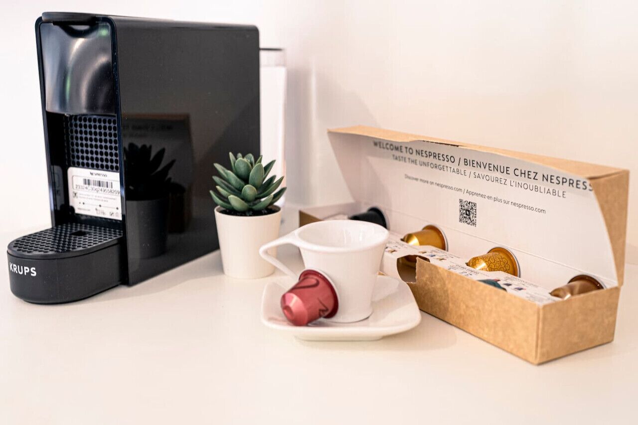 Eine Kaffeemaschine, ein Sukkulenten-Topf, eine weiße Tasse mit Untertasse und eine Kapselbox.