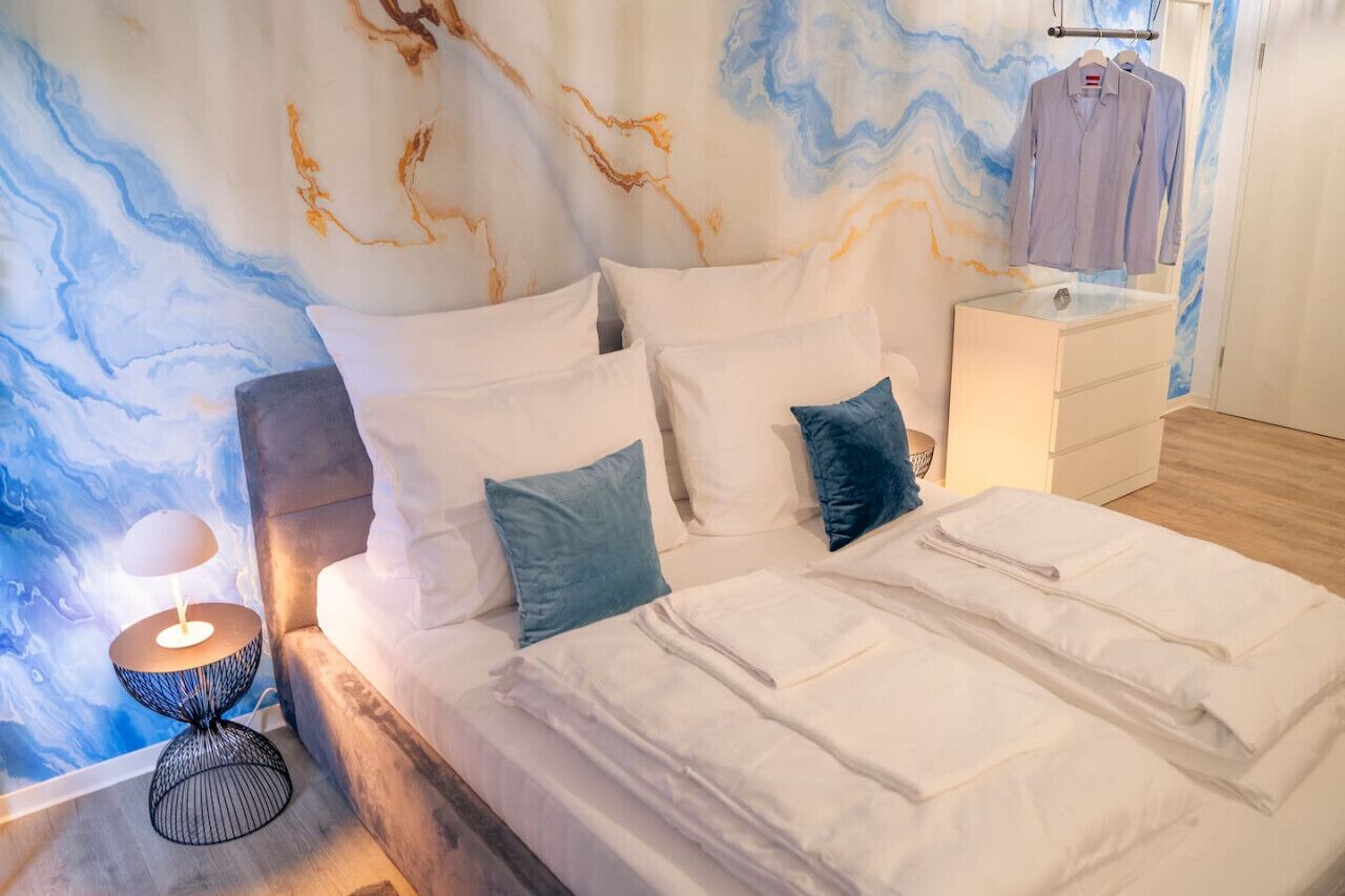 Ein ordentlich gemachtes Bett mit weißen Leinen, ein Nachttisch mit einer Lampe und eine Wand mit marmorartigem Dekor.