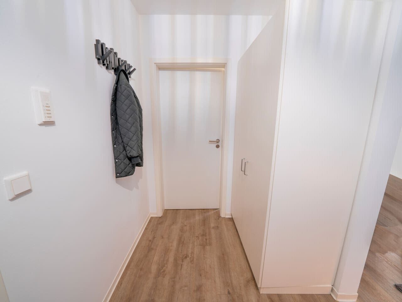 A hallway with a coat rack, a door, and a light switch.