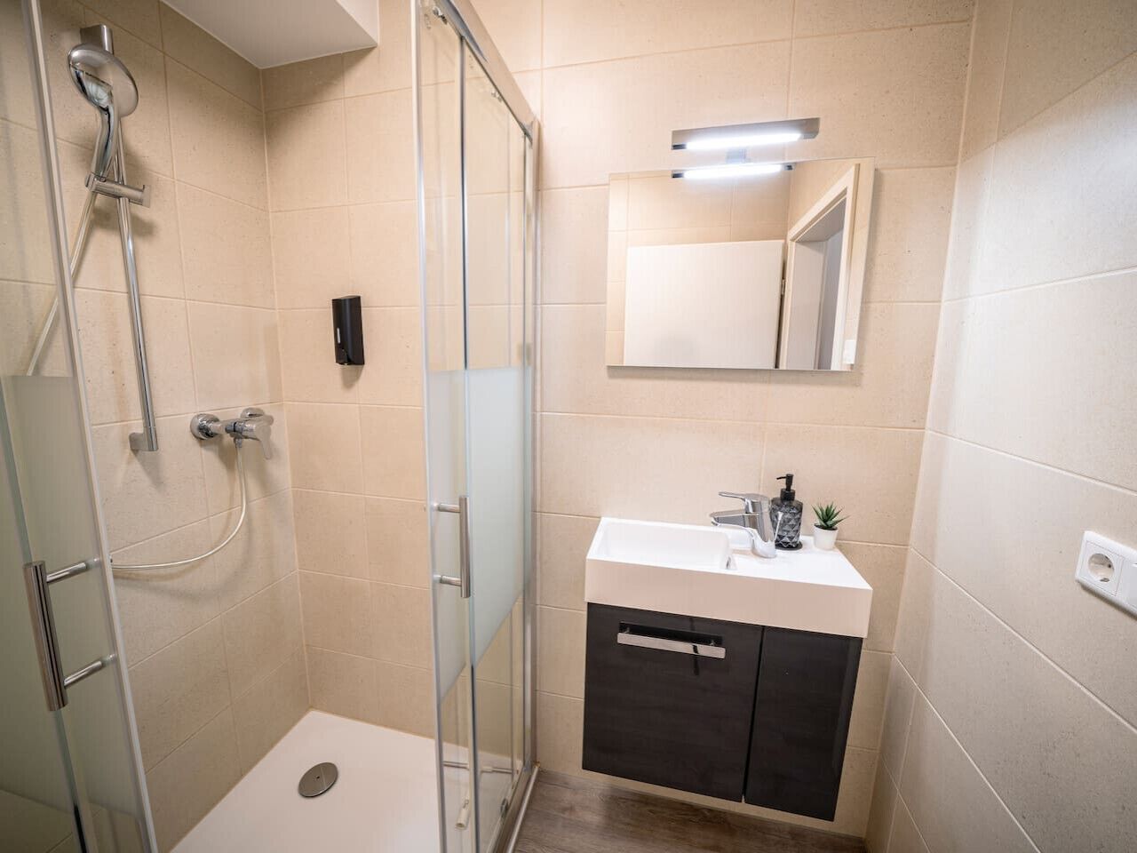 A modern bathroom with a glass shower enclosure, a white sink with a dark cabinet, and a mirror above the sink.