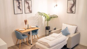 Une chambre à coucher de taille modeste, comprenant un lit, un bureau et une chaise. Trois œuvres d’art encadrées ornent le mur.