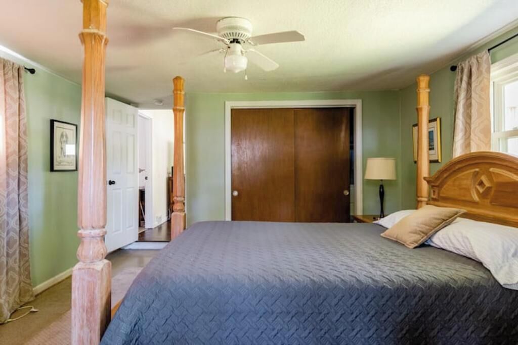Een slaapkamer met een bed, houten hoofdbord, plafondventilator en een deur.
