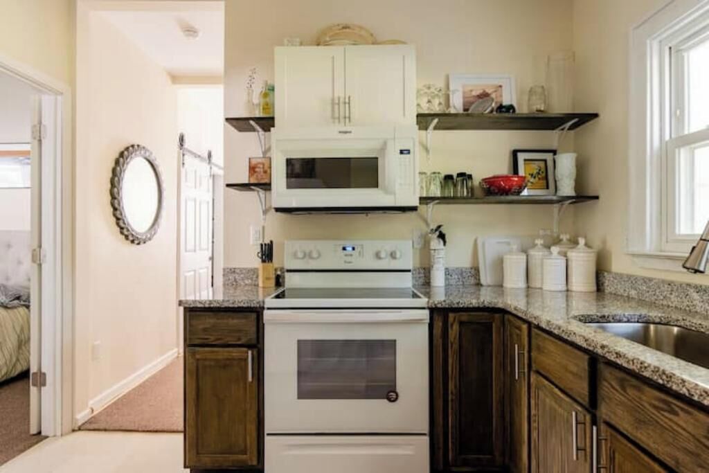 Une cuisine avec un four, un four à micro-ondes et une cuisinière blancs, des armoires en bois, des comptoirs en granit et une fenêtre.