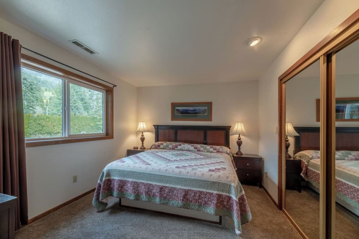 Un dormitorio con cama, dos mesitas de noche con lámparas, un espejo grande y una ventana con cortinas.