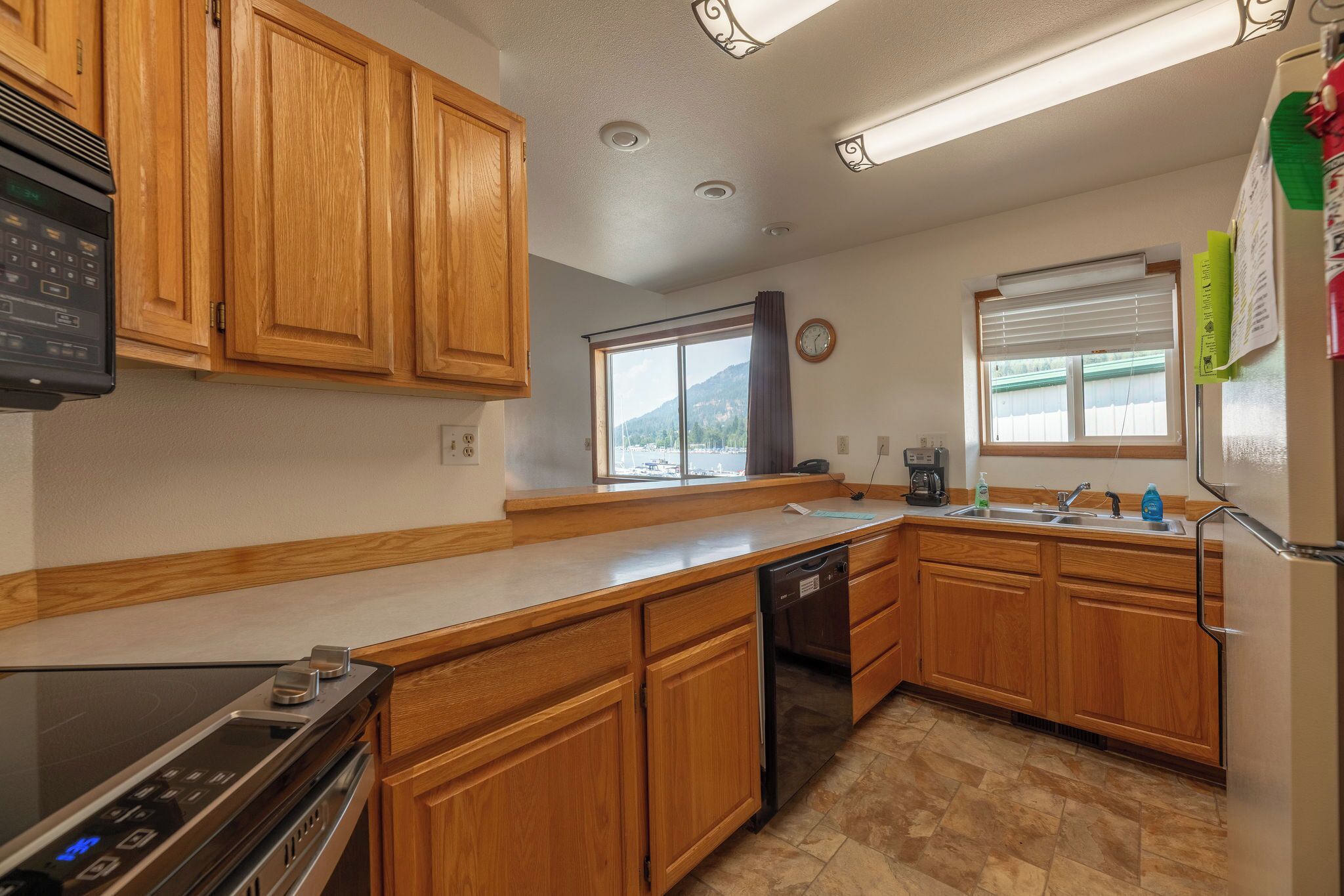 A kitchen with wooden cabinets, a built-in oven, a dishwasher, a window with a view of mountains, and a refrigerator.