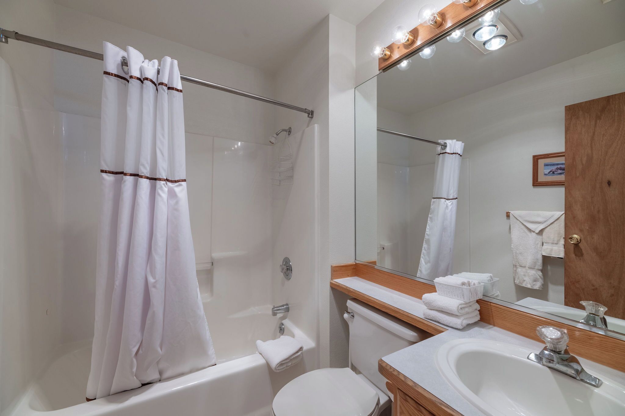 A modern bathroom with a glass-enclosed shower, a white toilet, a sink with a wooden countertop, and a large mirror.