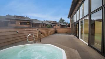 Un espace de bien-être comprenant un jacuzzi, une terrasse en bois et un bâtiment doté de grandes fenêtres.
