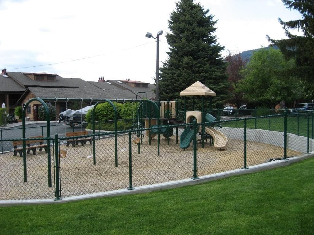 A fenced playground with a slide, climbing structures, and benches.