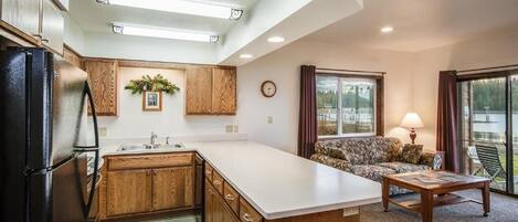 A kitchen with wooden cabinets, a refrigerator, a large island, and a dining area with a sofa and table.