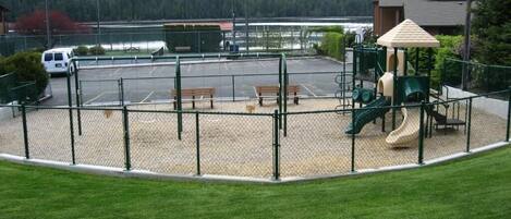 A fenced playground with a slide, benches, and a small shelter.