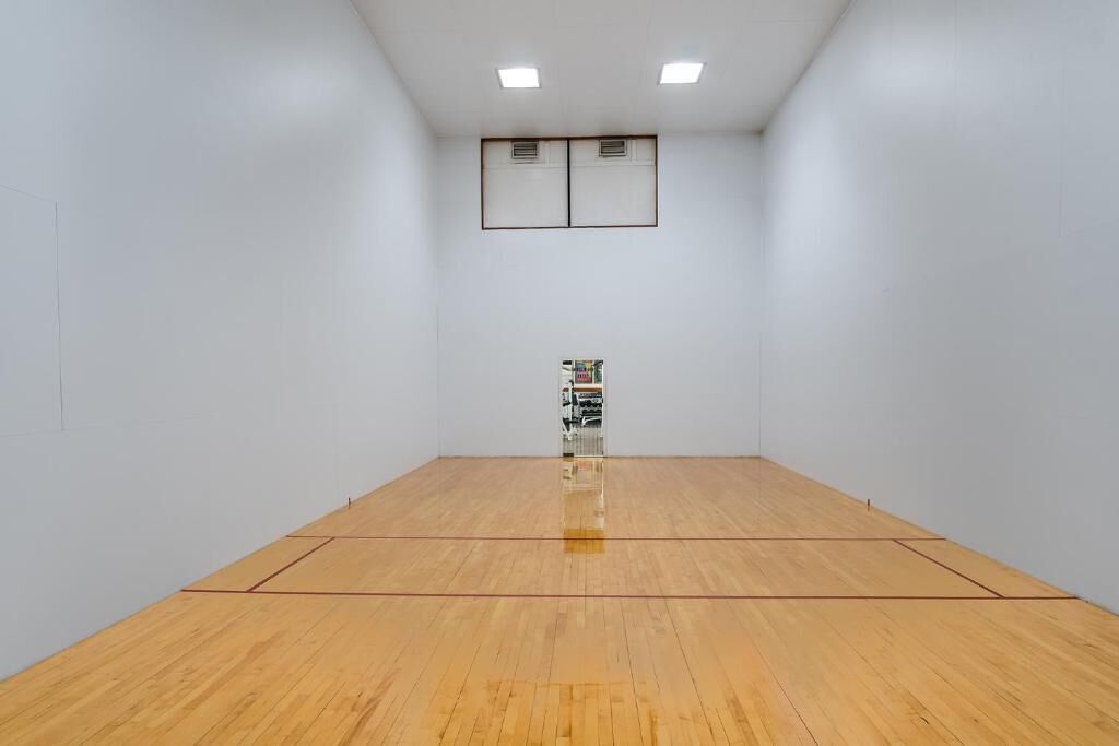 A squash court with a wooden floor, white walls, and two ceiling lights.