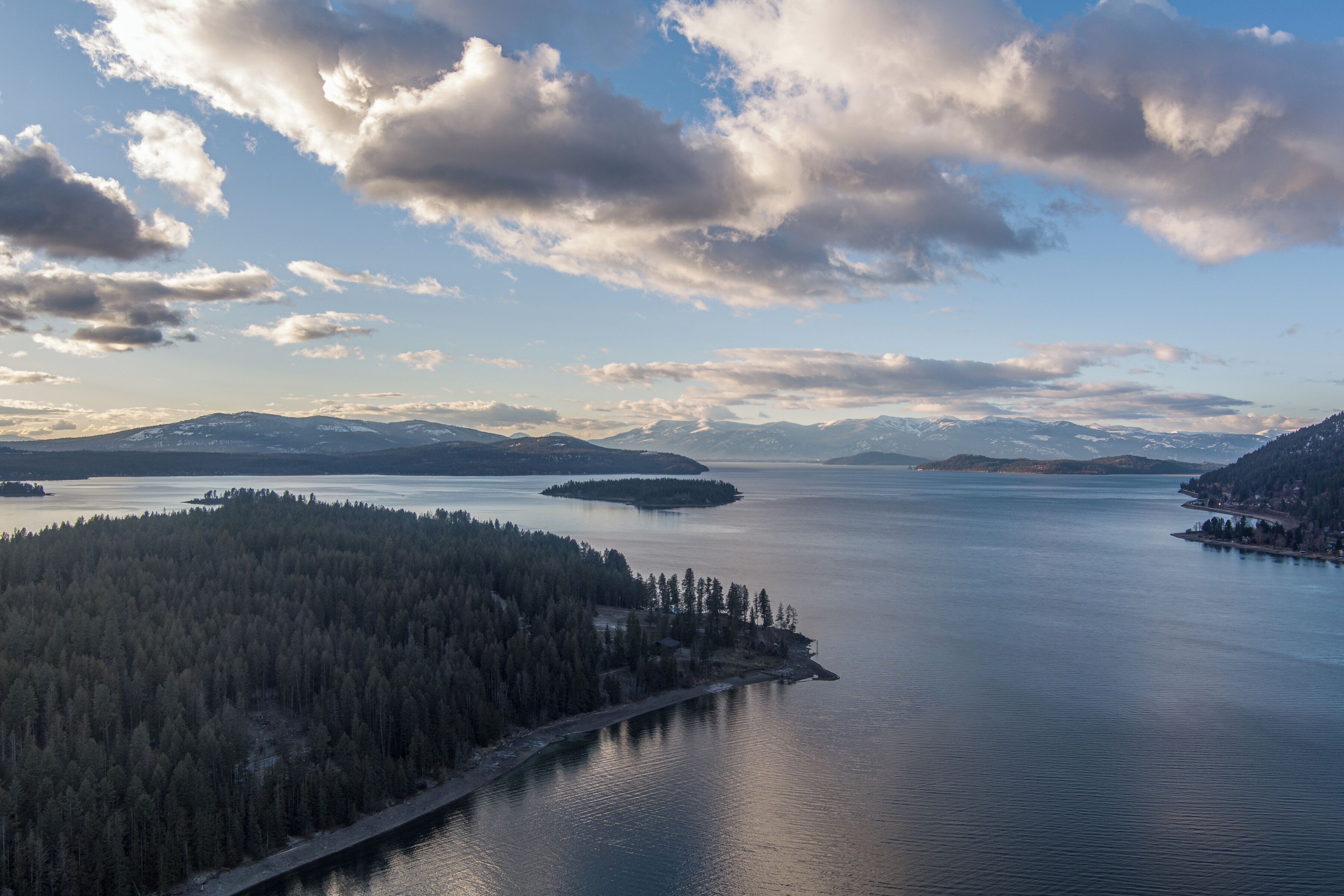 Une vue panoramique d’un lac entouré de collines et de montagnes boisées.