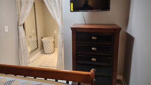 A bedroom with a wooden dresser, a television mounted on the wall, and a bed with a headboard. - Cozy, beautiful apartment with lots of amenities! 3 miles from downtown fun! (Columbus)