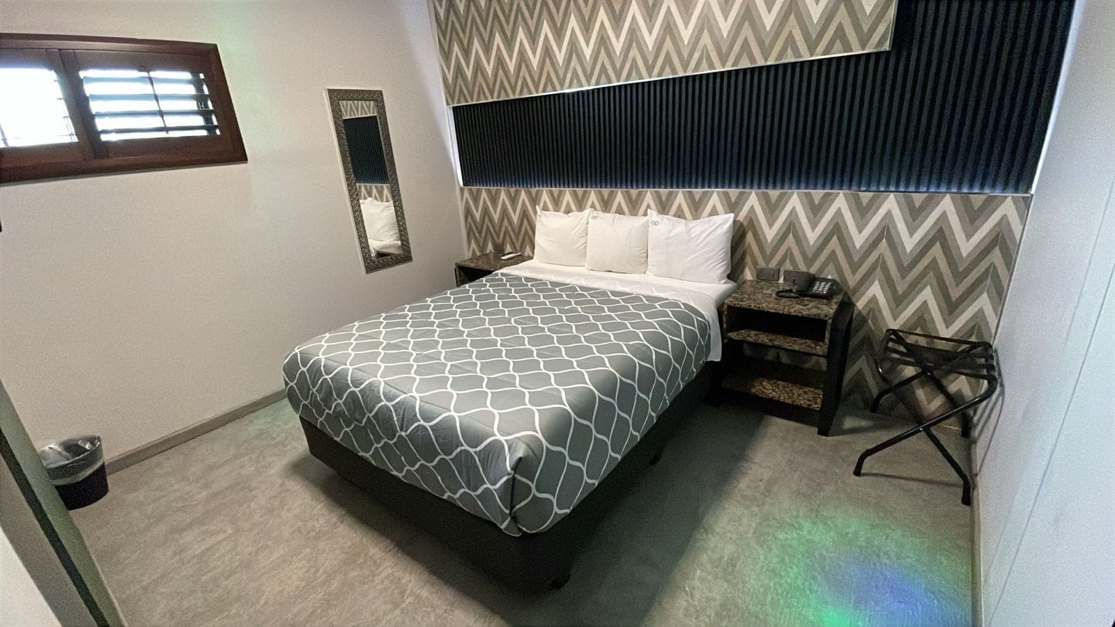 Un dormitorio con cama, mesitas de noche, un espejo y una ventana.
