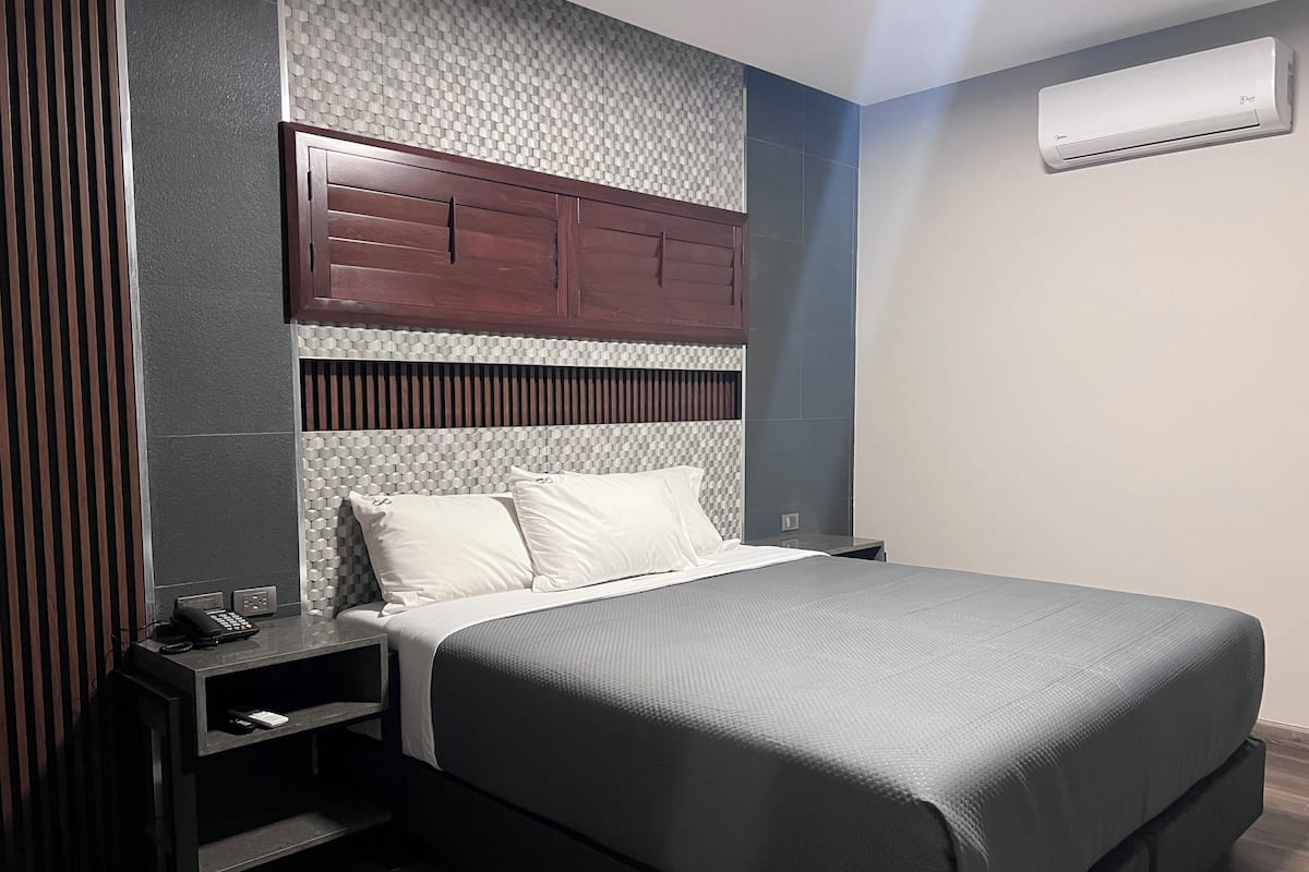 Un dormitorio moderno con una cama grande, un cabecero de madera, una mesita de noche y un equipo de aire acondicionado en la pared.