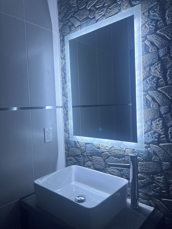 A bathroom with a white sink, a mirror, and a stone-patterned wall.