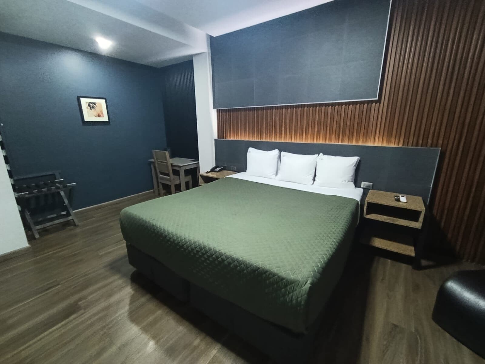A hotel room with a bed, a desk, a chair, a nightstand, and a picture on the wall.