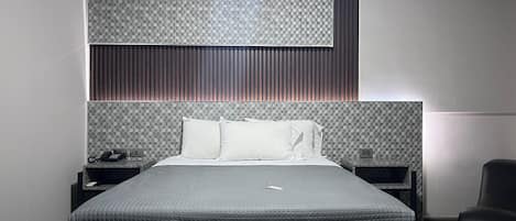 Una camera da letto moderna con un letto grande, una testiera con motivo decorativo, un comodino con un telefono e una sedia.