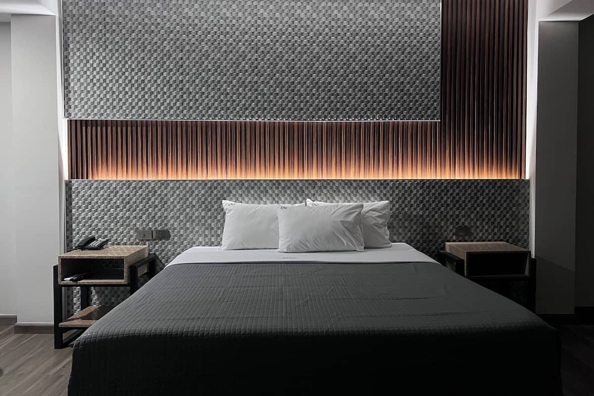 Una habitación de hotel moderna con una cama grande, una mesita de noche y una pared con textura y listones verticales.