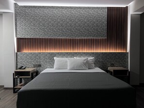 Ein modernes Hotelzimmer mit einem großen Bett, einem Nachttisch und einer Wand mit einer strukturierten Oberfläche und vertikalen Lamellen.