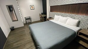 Ein Hotelzimmer mit einem großen Bett, einem Nachttisch, einem Schreibtisch und einem Stuhl.