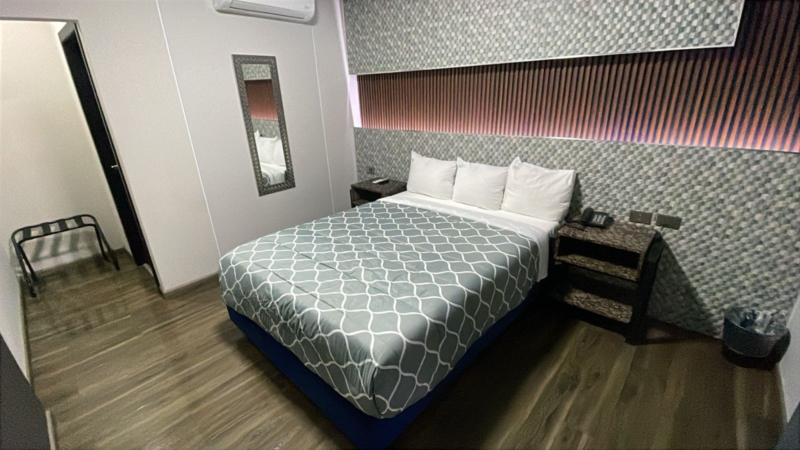 A hotel room with a bed, bedside tables, a mirror, and a wall with a textured pattern.