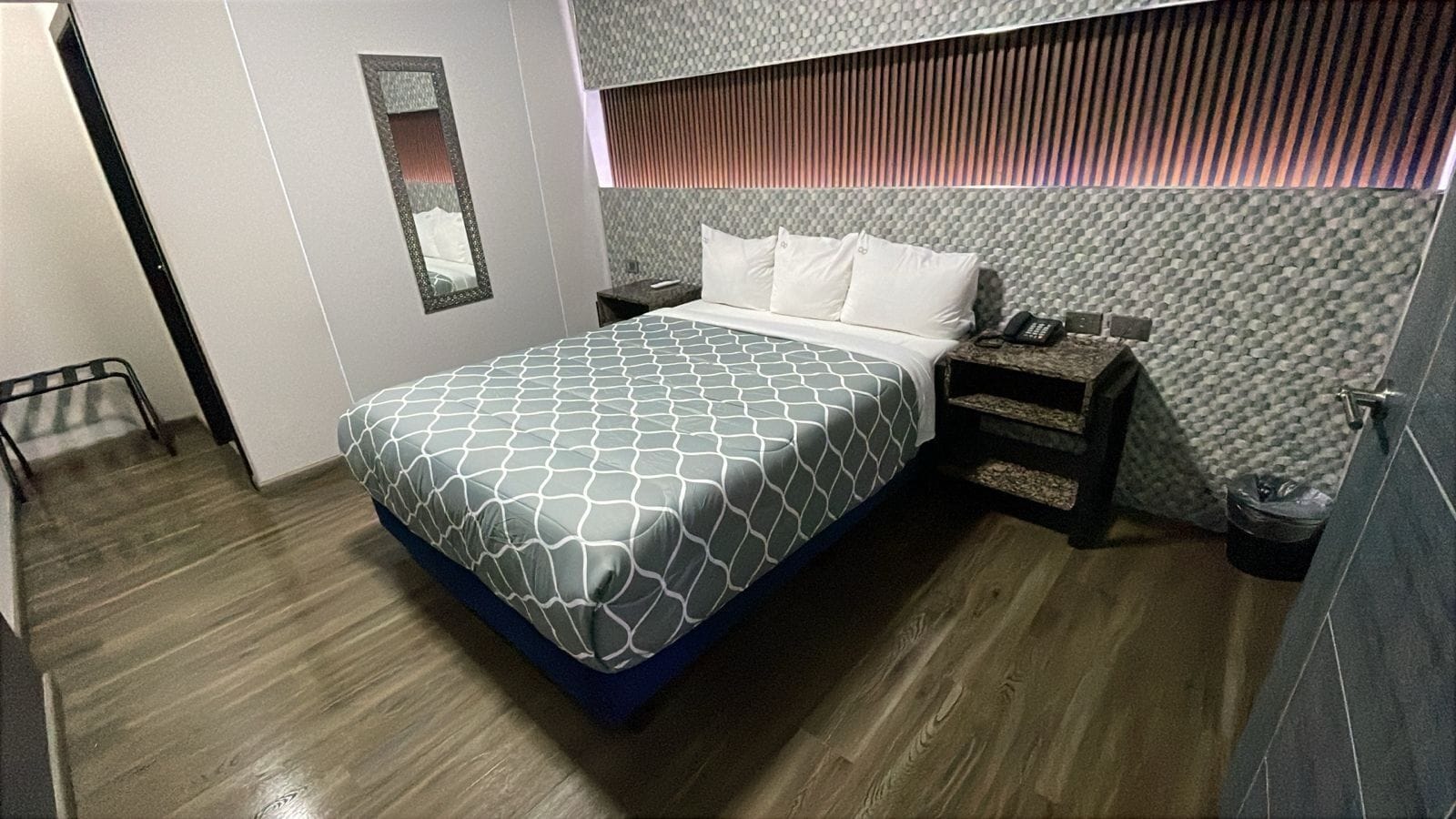 Une chambre d’hôtel moderne avec un grand lit, une table de chevet, un miroir et un mur à motifs.